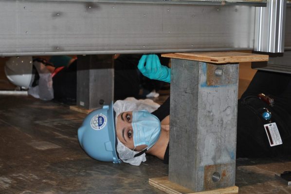 A woman wearing a hard hat and a mask while preparing the anode plane assembly, a major component of the short-baseline near detector, for installation at Fermilab.