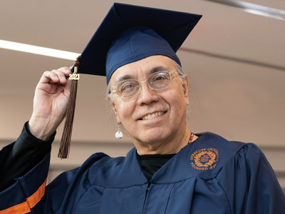 A Native American man poses for a photo in his Commencement cap and gown.