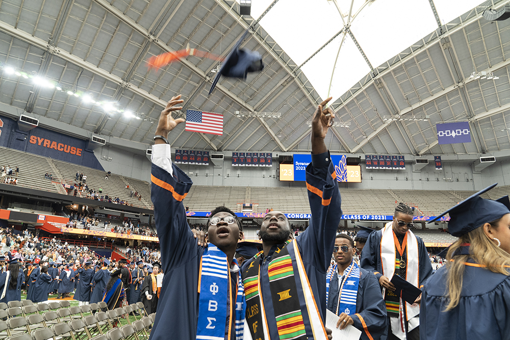 Two students toss their mortarboards in the air at Commencement 2023