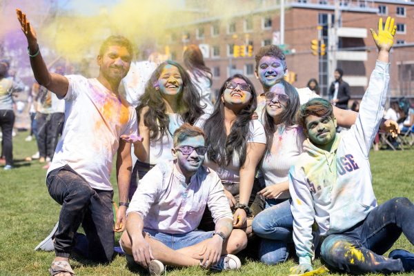 Group of students sitting together in white shirts colored in various colors.