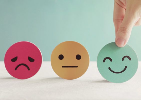 stock image of three cut-outs of a sad face, neutral face, and happy face