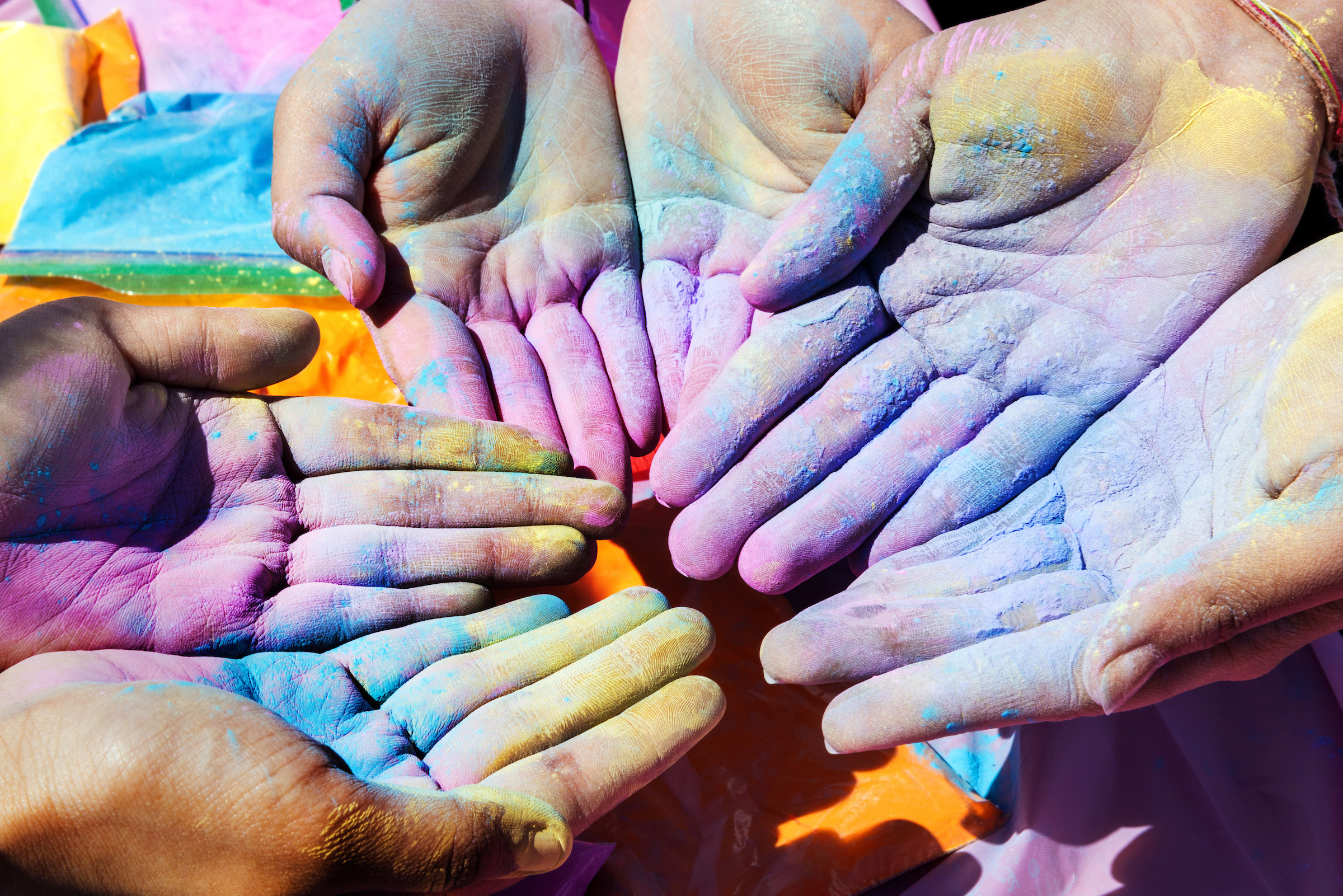 Several individuals holding the palms of their hands together covered in various colors.