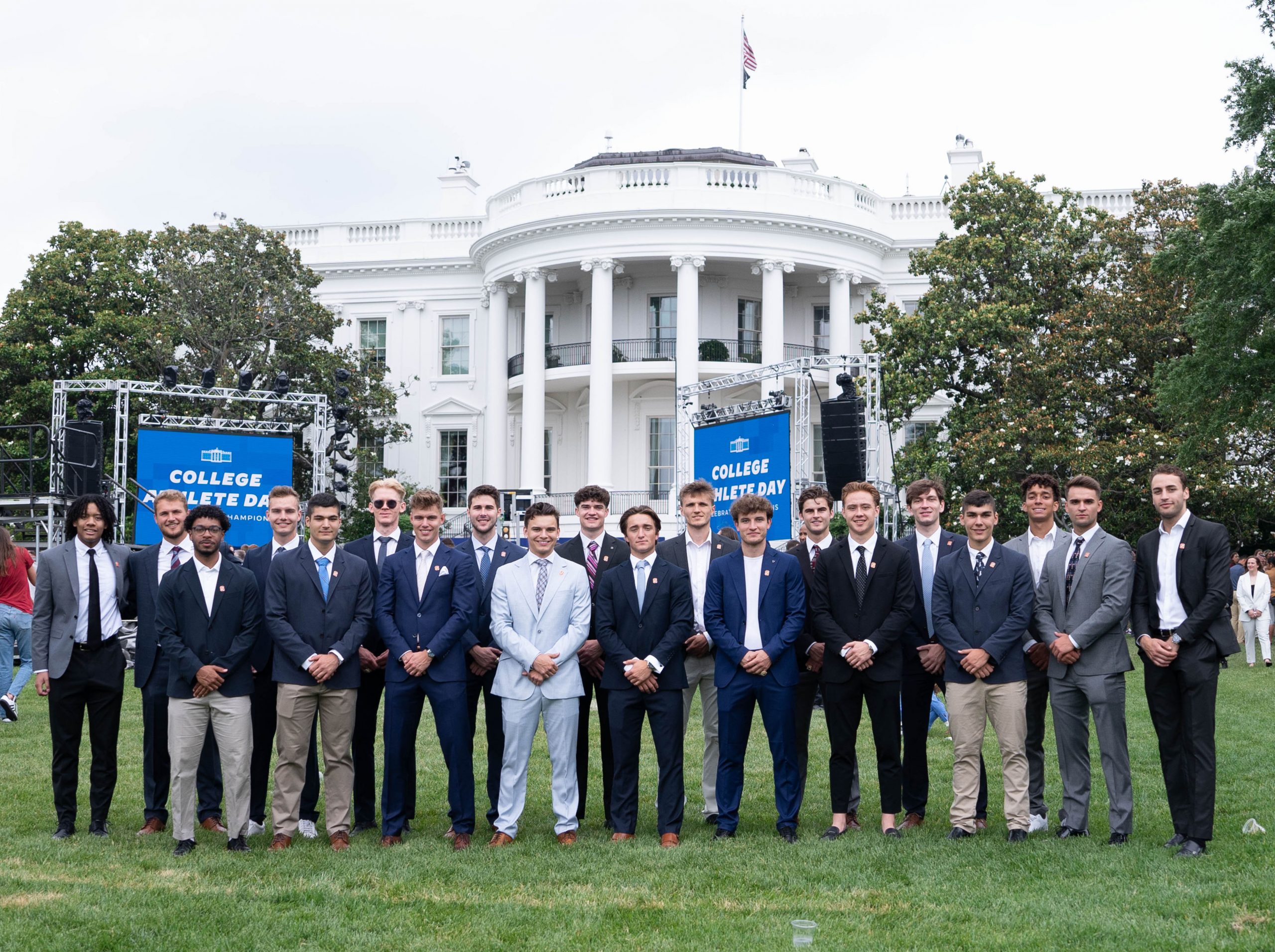 Men's soccer team all dressed in suits standing on the lawn in front of the White House. 