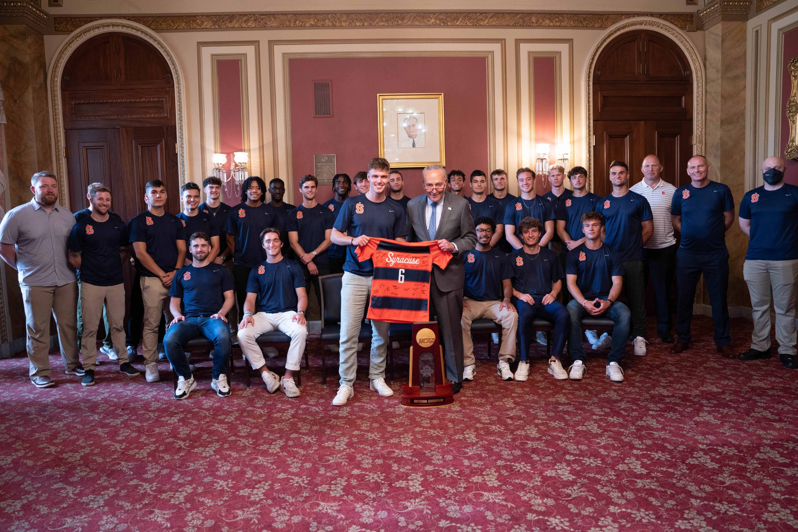 Men's soccer team posing with Charles Schumer at the Capitol. 
