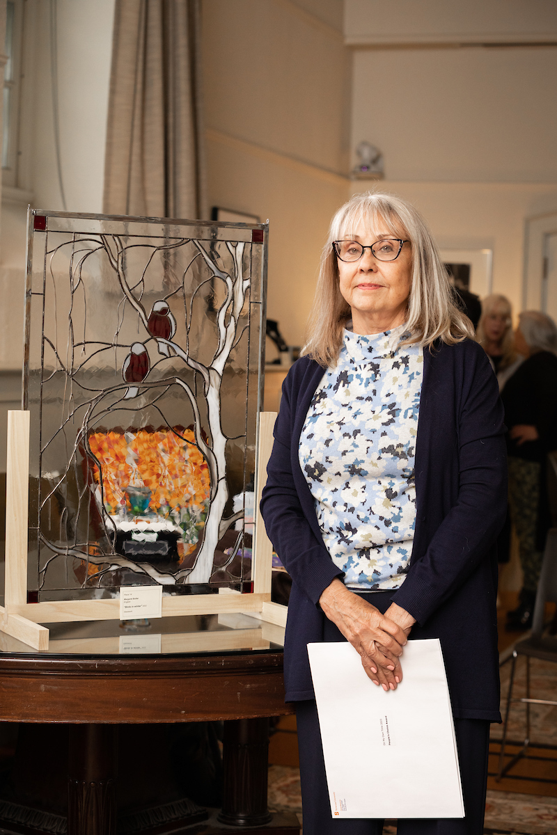 Staff member Margaret Butler poses next to her glasswork piece titled "Birds in Winter"