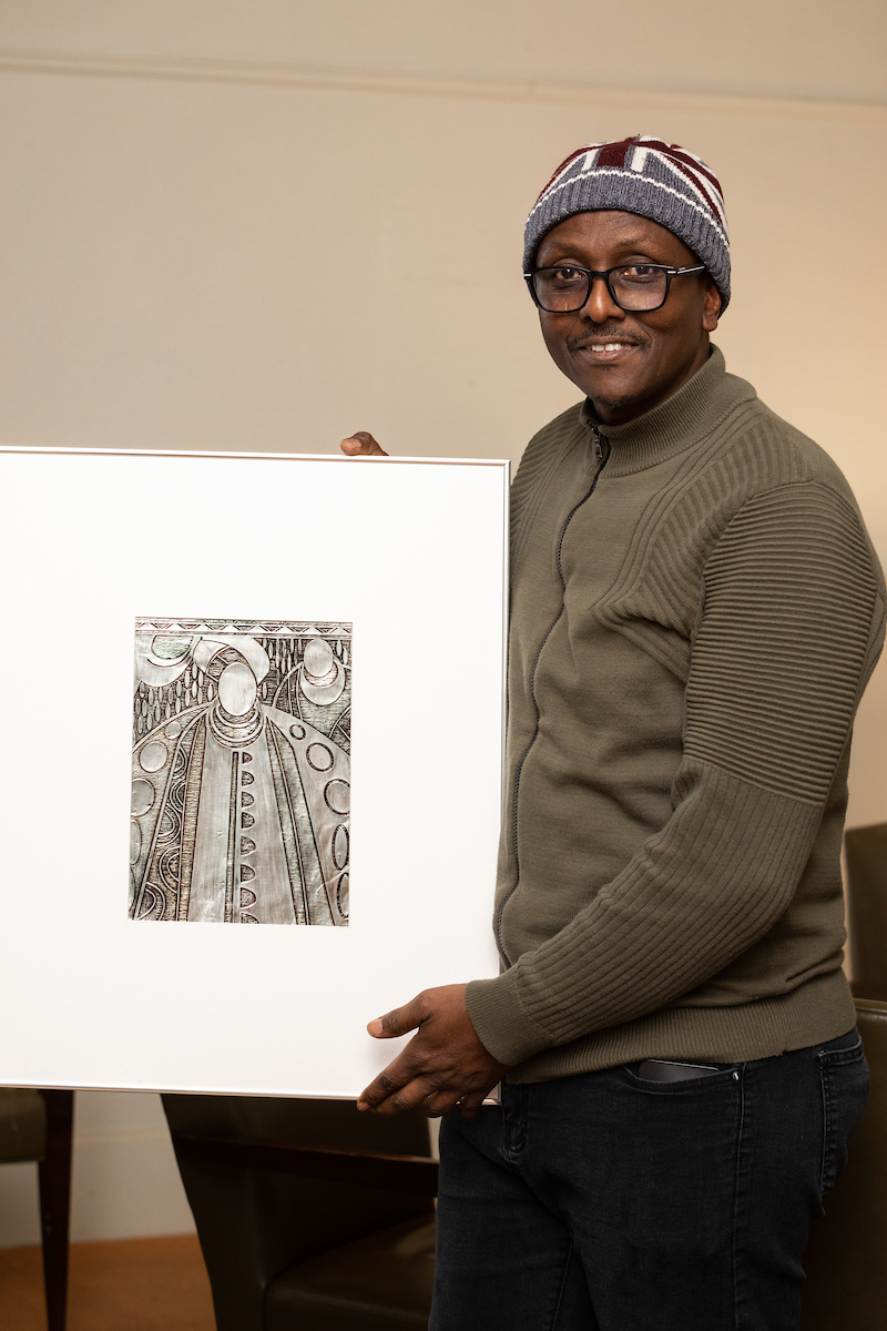 Austine Emifoniye poses with his artwork "Royal Procession" at the "On My Own Time" reception