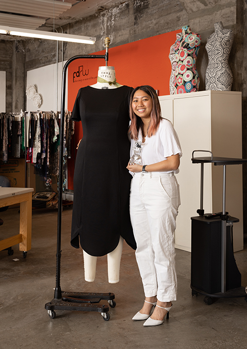 Individual standing with a mannequin wearing a black dress.