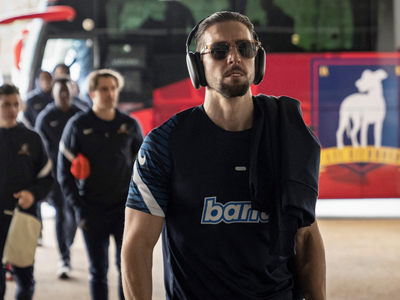A man wearing sunglasses, a soccer jersey and headphones walks alongside his teammates during a scene in "Ted Lasso."