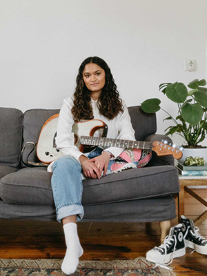Individual sitting on a couch with a guitar in their lap.