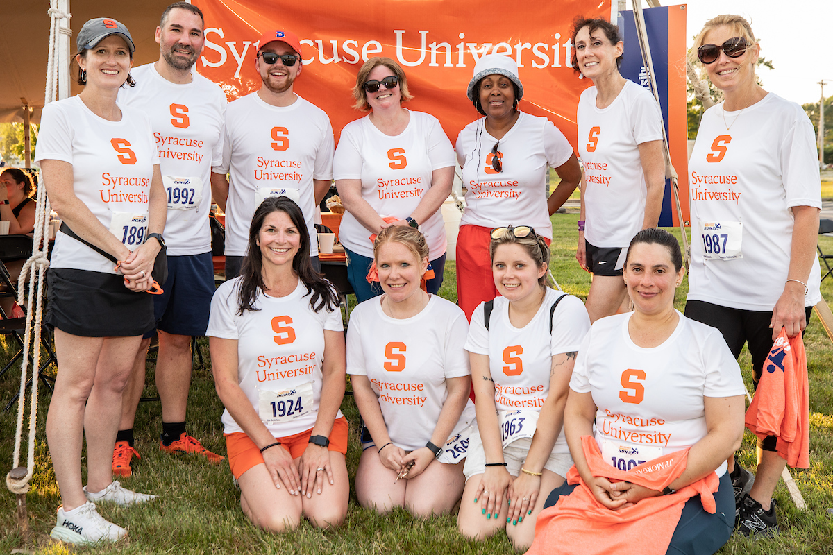 participants at the 2023 WorkForce Run gather together for a photo in front of a Syracuse University banner