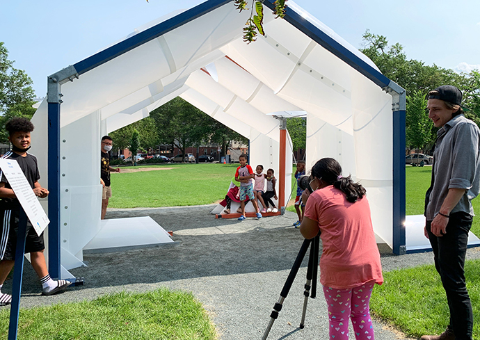 Person outside taking a photo with a camera on a tripod of a white tent with children inside