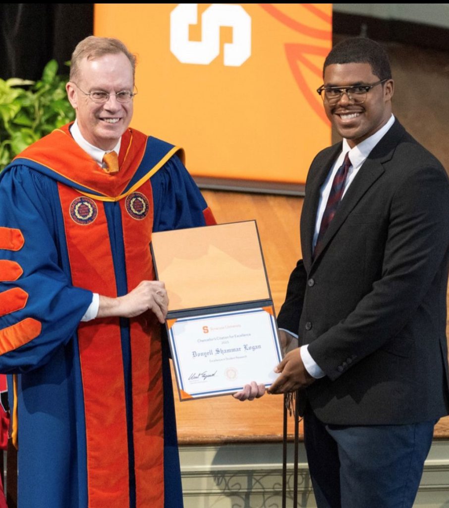man in commencement robe hands certificate to man in suit at an award ceremony