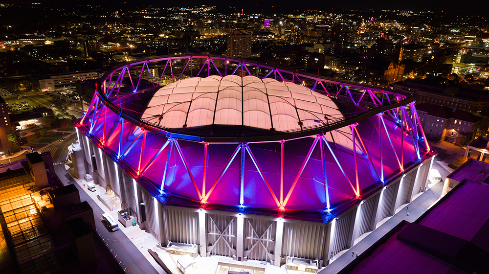 aerial photo of JMA Wireless Dome on the Syracuse University campus lit up in blue and orange at night