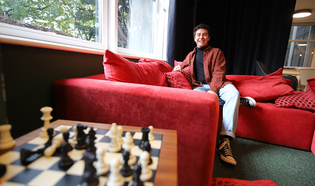 Individual sitting on a red couch in the background with a chess game in the foreground.