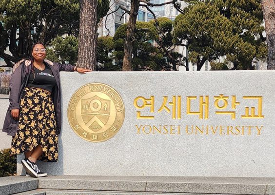 A woman poses for a photo in front of the main sign at Yonsei University in Seoul, South Korea.