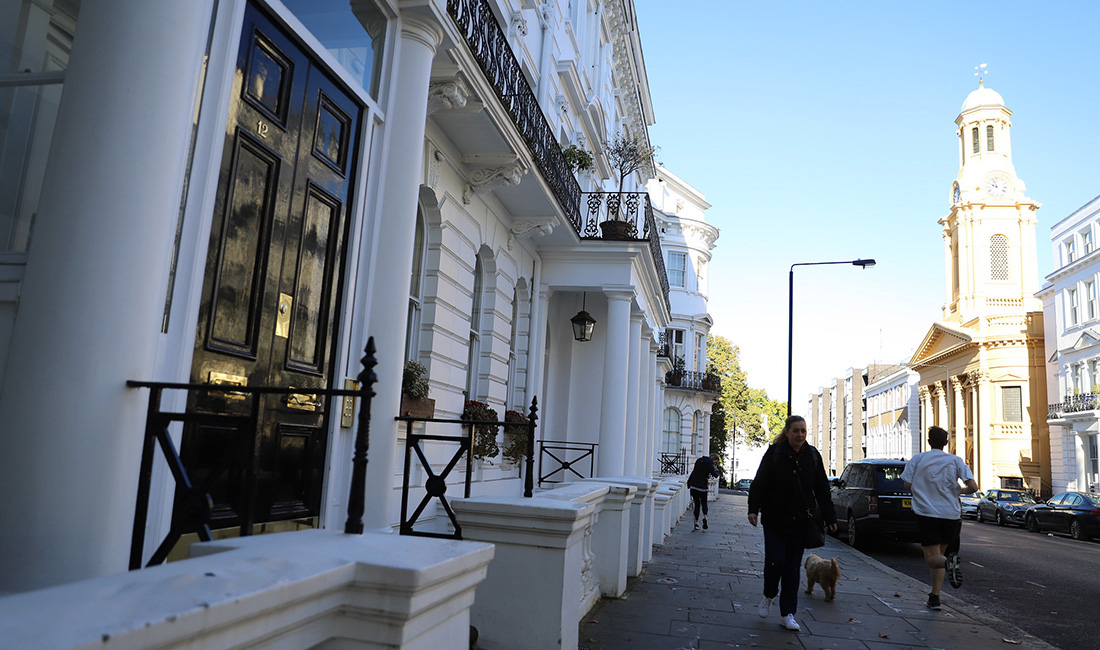 Person walking down a street in London with their dog on a blue sky day