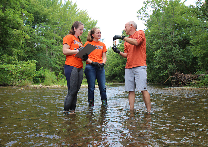 Three people in orange tshirts standing in water conducting testing