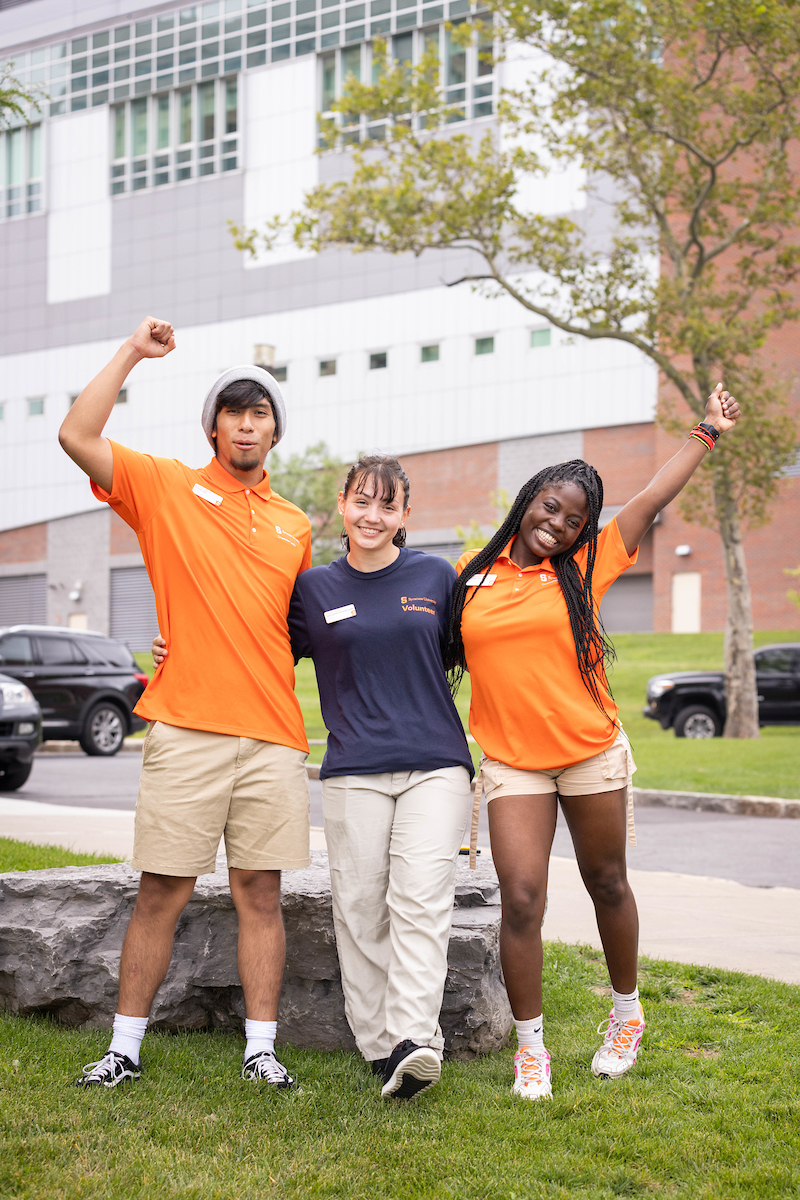 Three students pose together outside of a residence hall during move-in