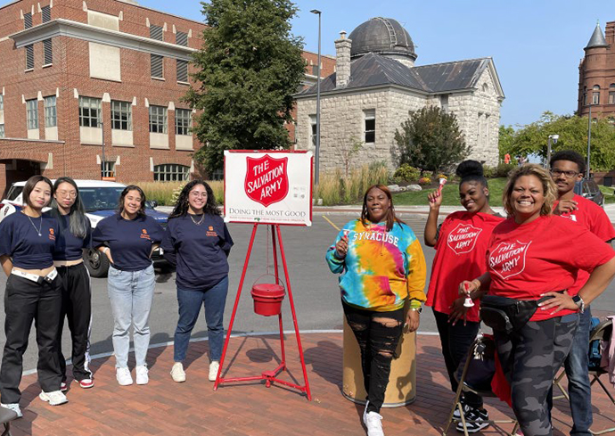 Group of people standing outside on campus with a Salvation Army red kettle donation bucket