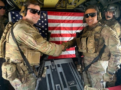 Two servicemen on helicopter in front of American flag