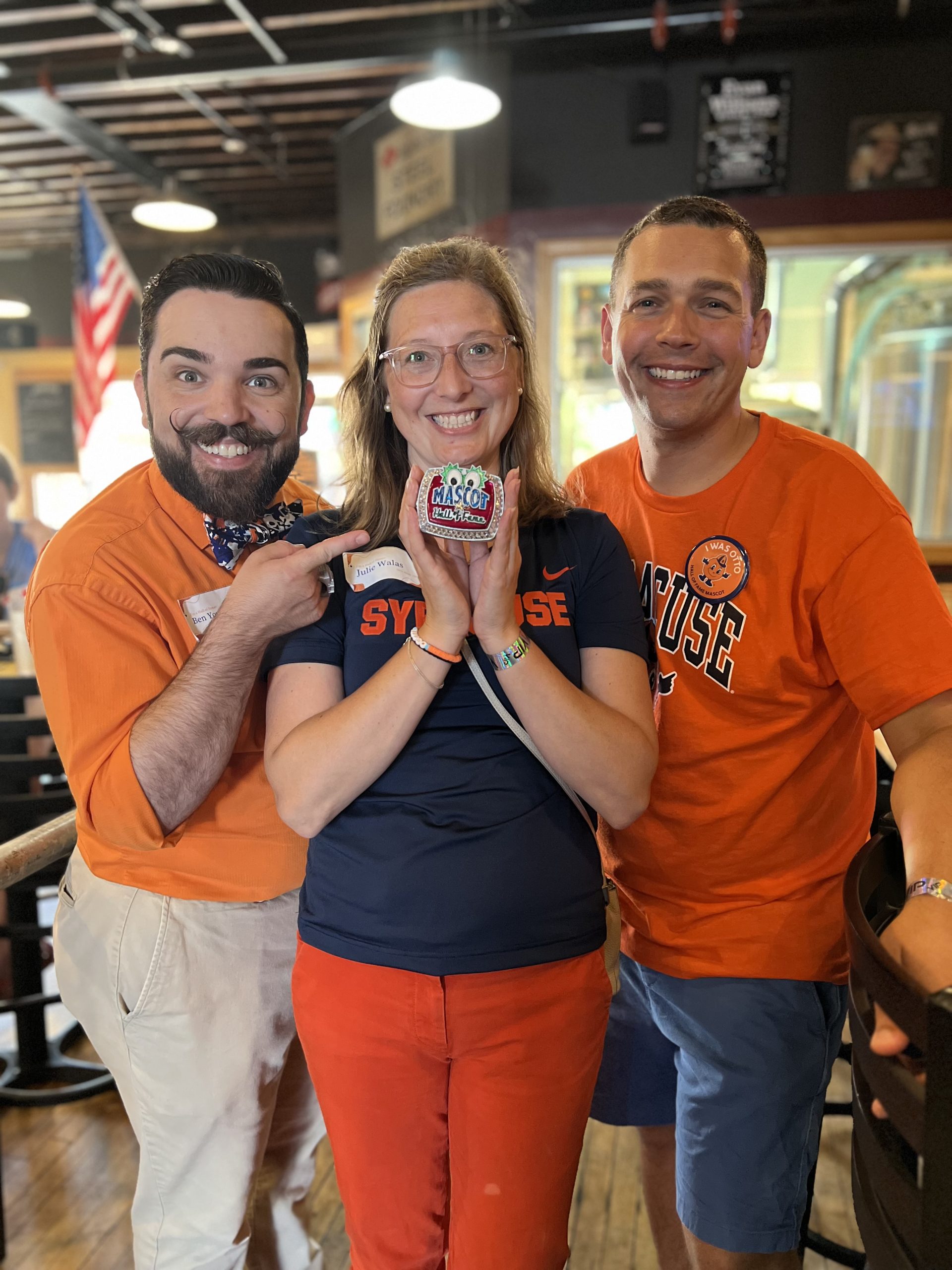 Three individuals standing together with the center person holding Otto's Hall of Fame ring. 