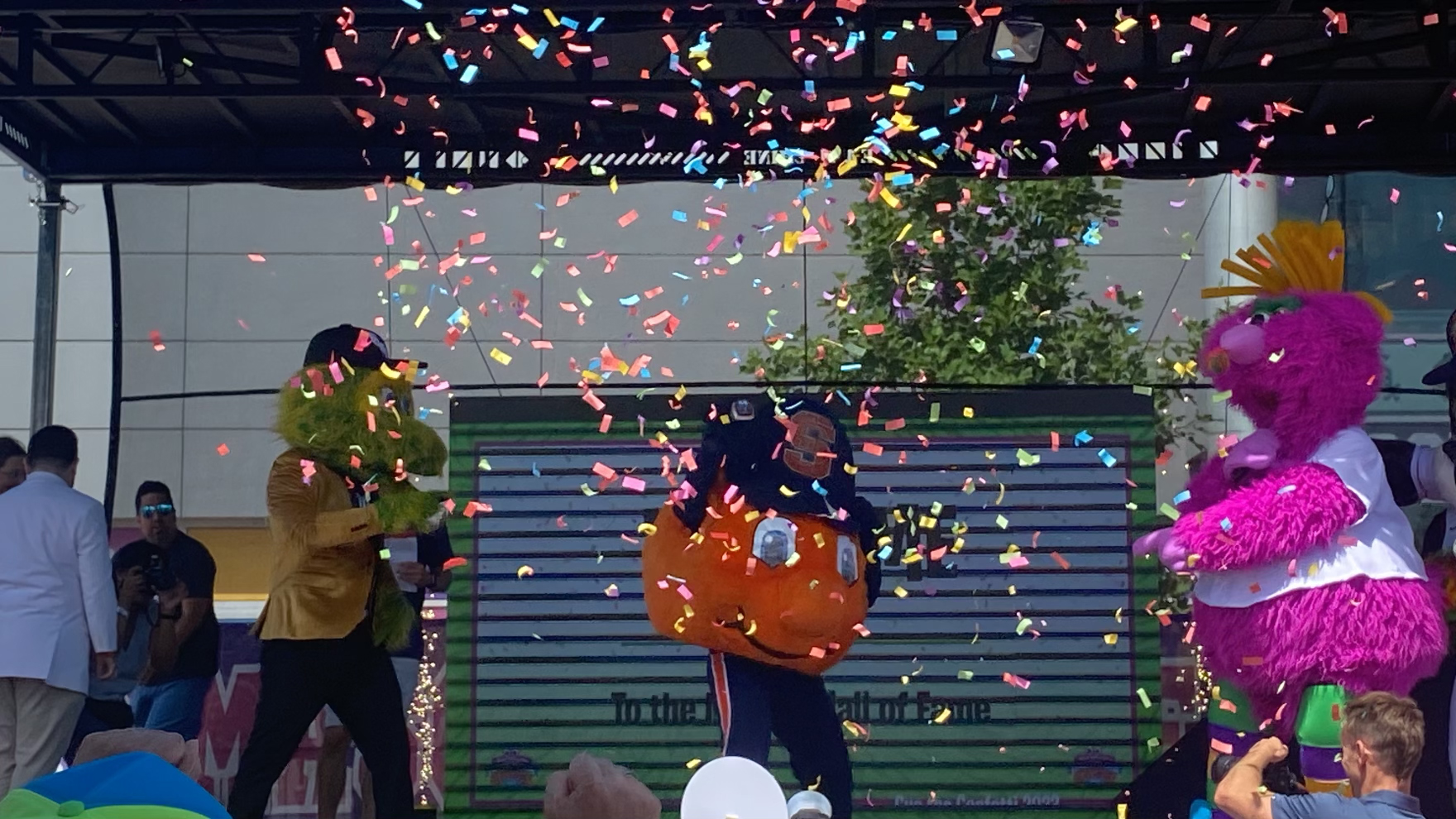 Otto the Orange on the stage with other mascots spraying them with confetti. 