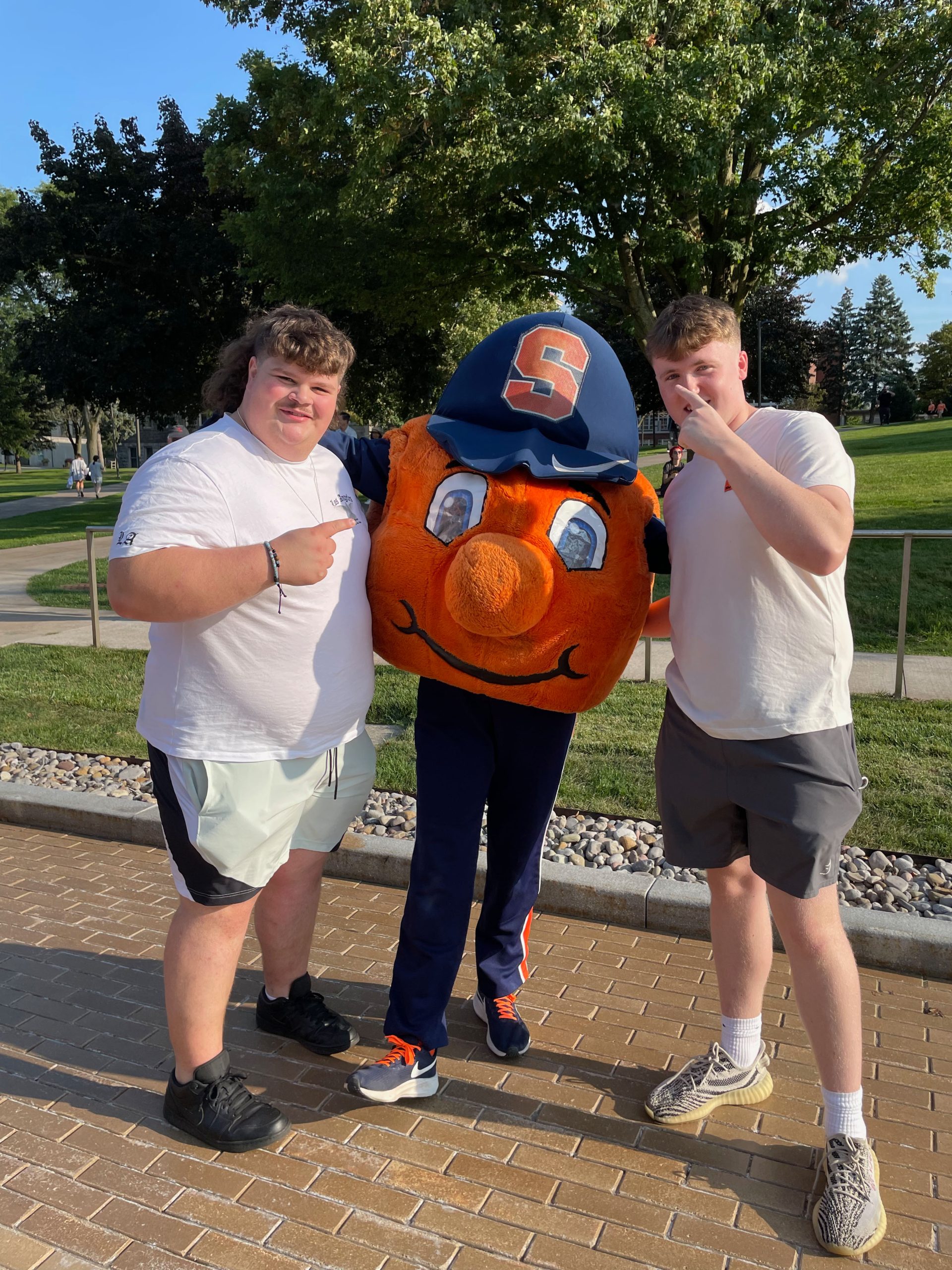 Two individuals standing with Otto the orange on the promenade 