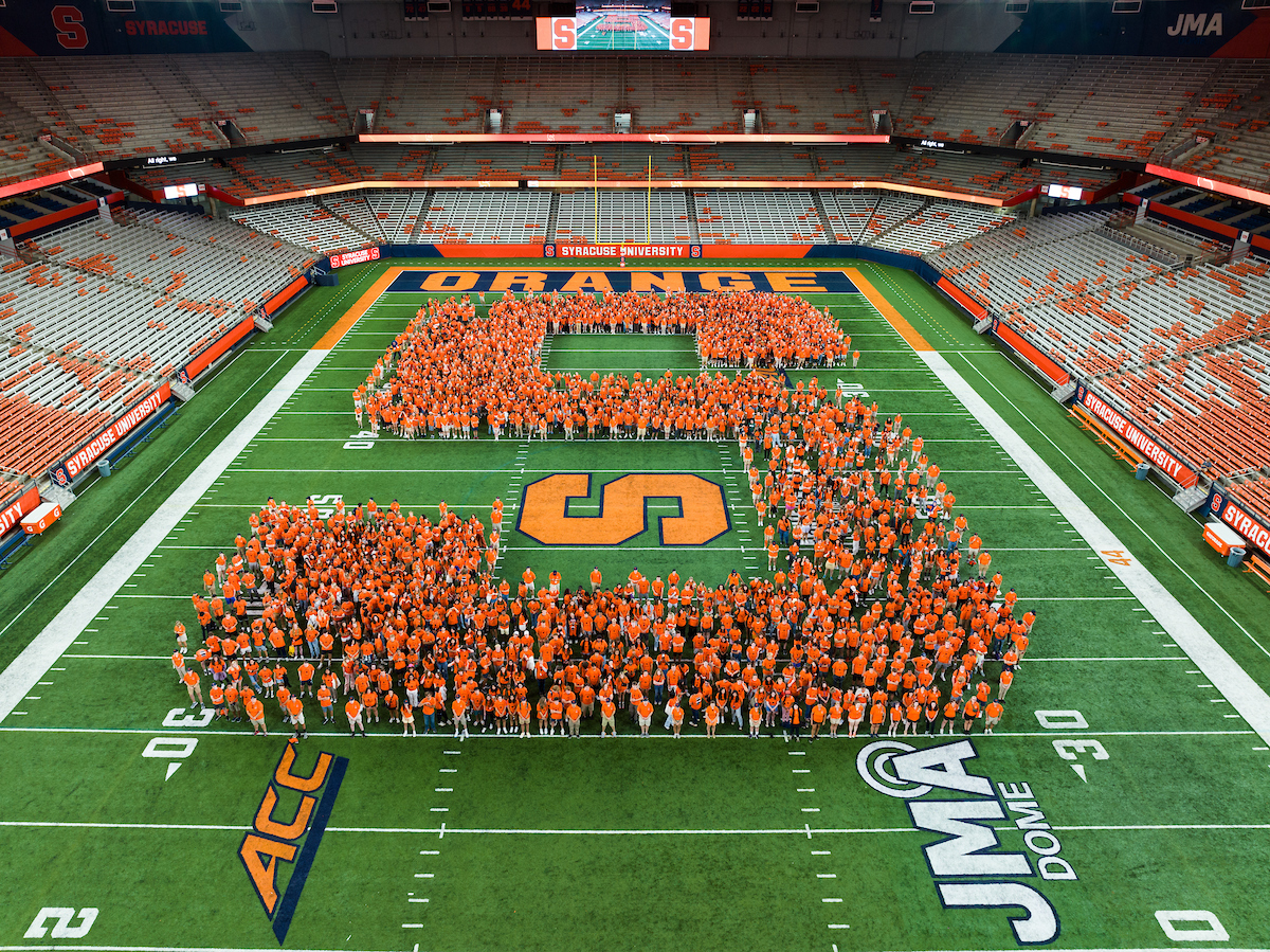 Students wearing orange form a giant S on the field of the JMA Wireless Dome