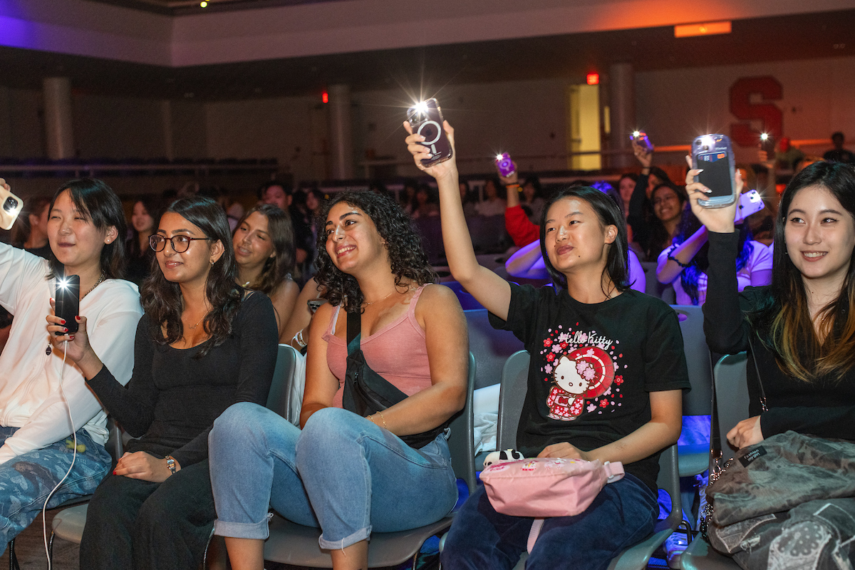 students in an audience hold up their cell phones with the flashlight on