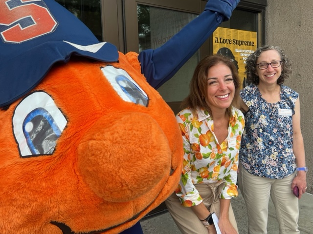 Two individuals pose for a selfie with Otto the Orange