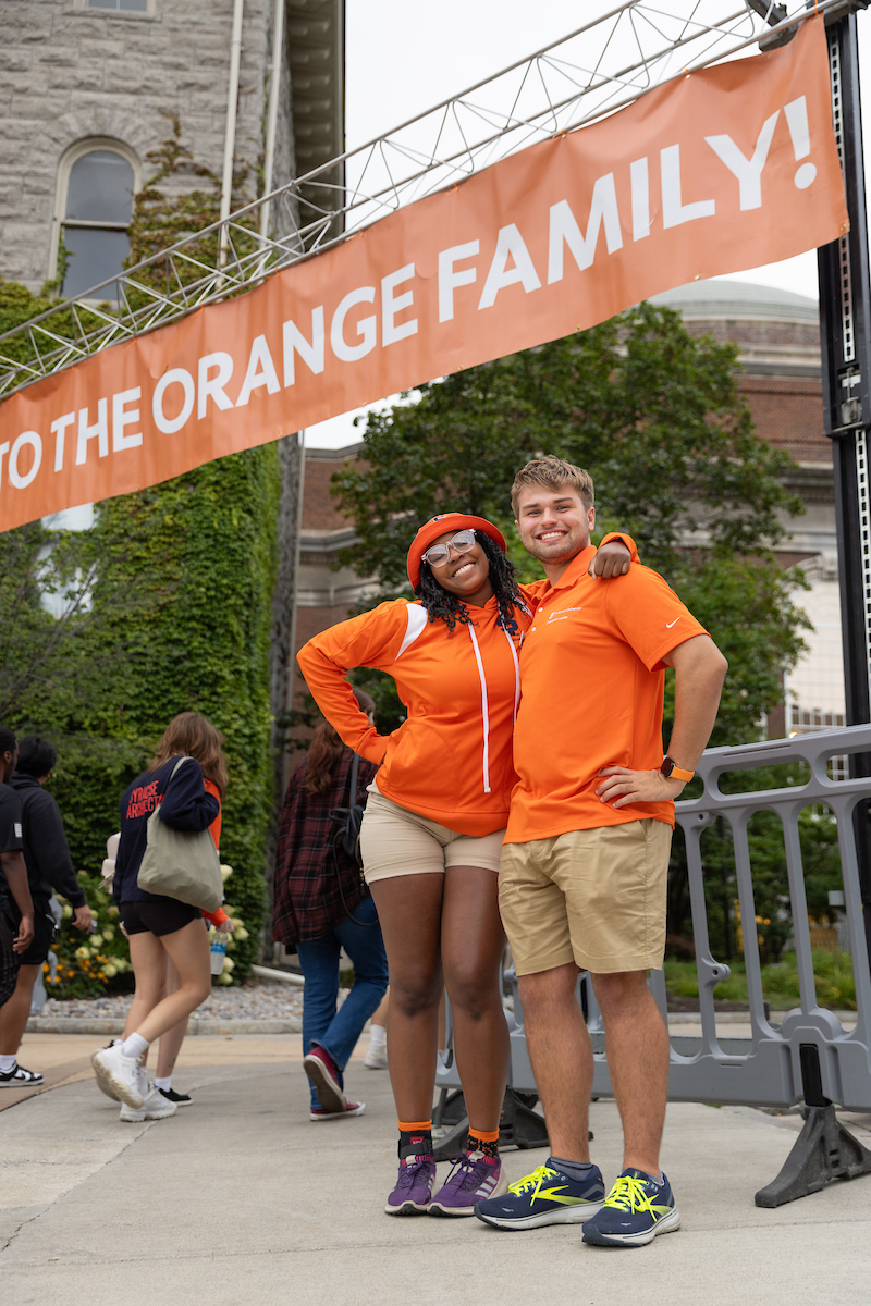 Two students pose together under a banner that says "Welcome to the Orange Family!"