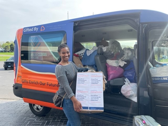 Individual holding a box of items to donate next to a van loaded with other items to be donated.