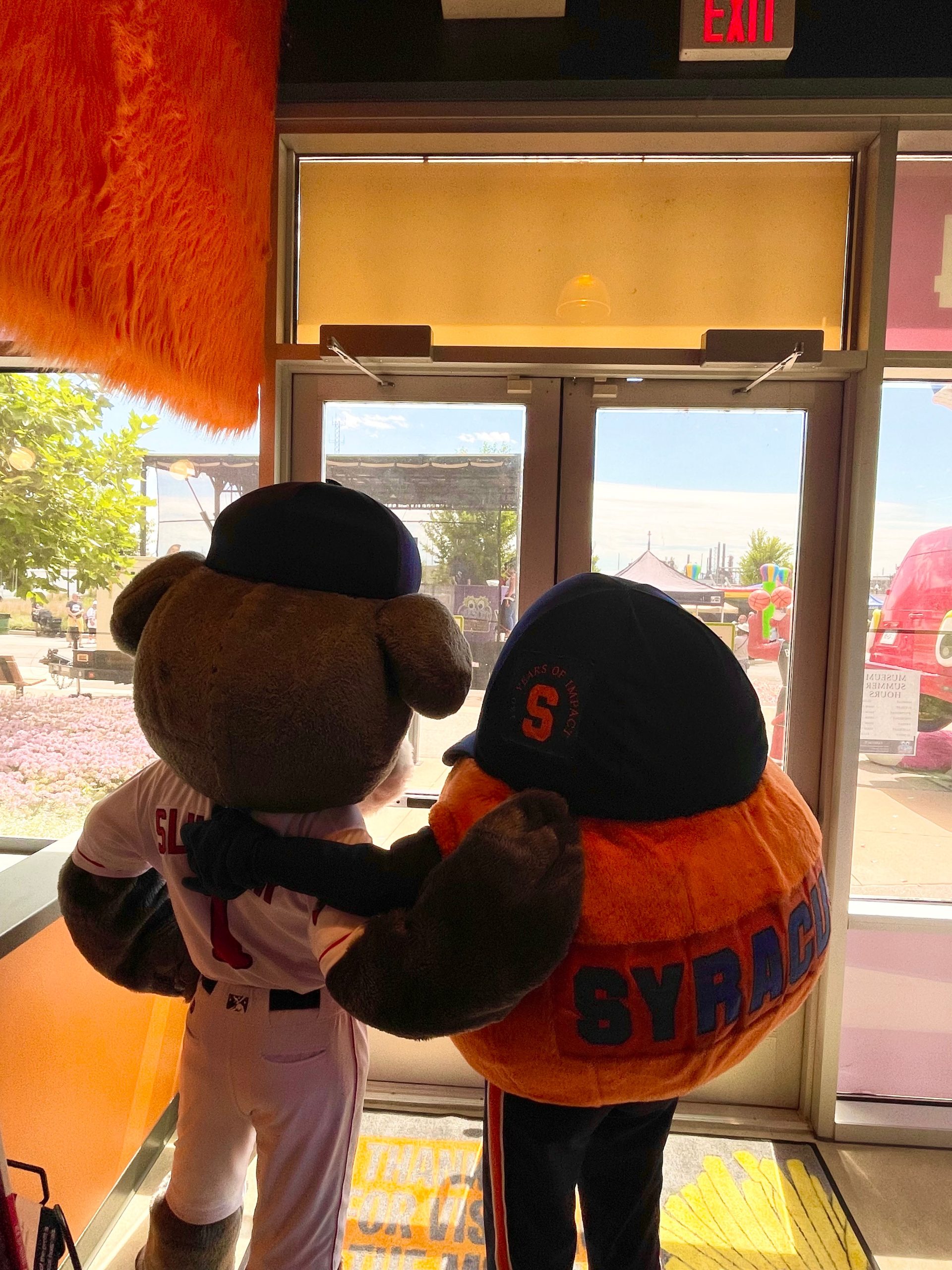 Slugger the Sea Dog and Otto the Orange standing arm and arm waiting to go through a set of double doors.