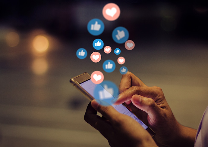 stock image of person using social media on a mobile device with like and heart bubbles popping up