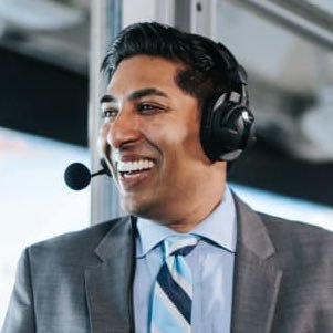 A man smiles while broadcasting a Carolina Panthers football game from the press box.