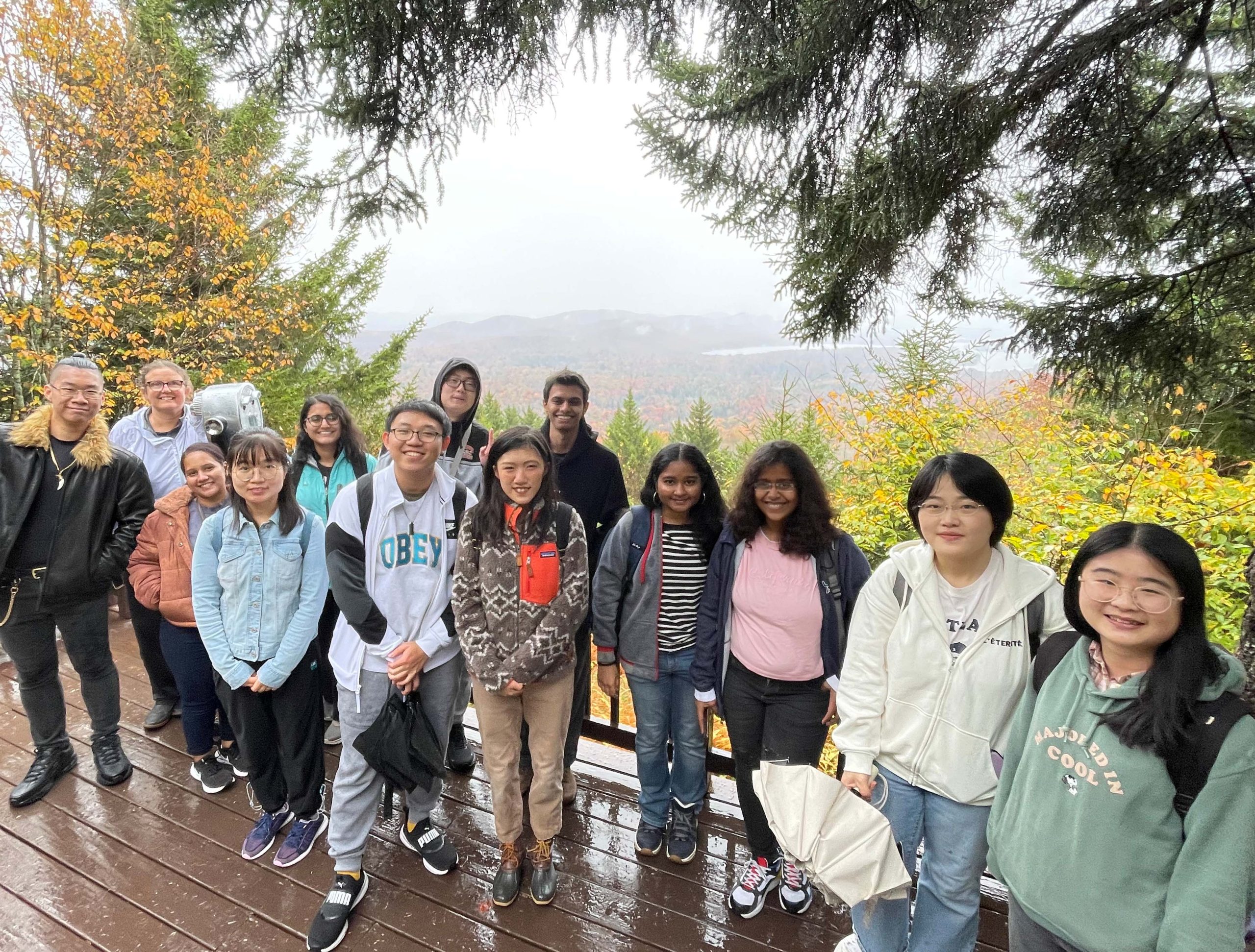Group of students standing a deck in the with beautiful fall colors on the trees in the background.