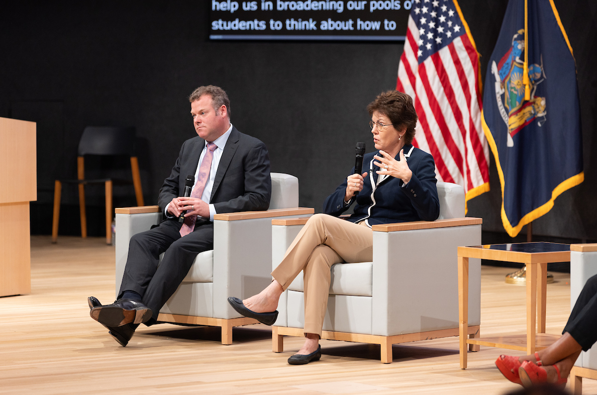 Two individuals sitting on stage speaking during a panel discussion.