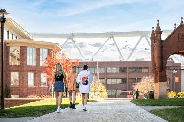 Three students walk towards the Stadium past Maxwell and Crouse College.