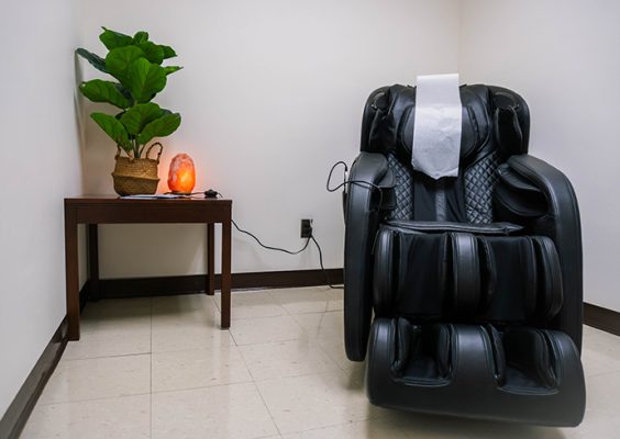Large black massage chair with a table next to it with a salt lamp and plant on it.