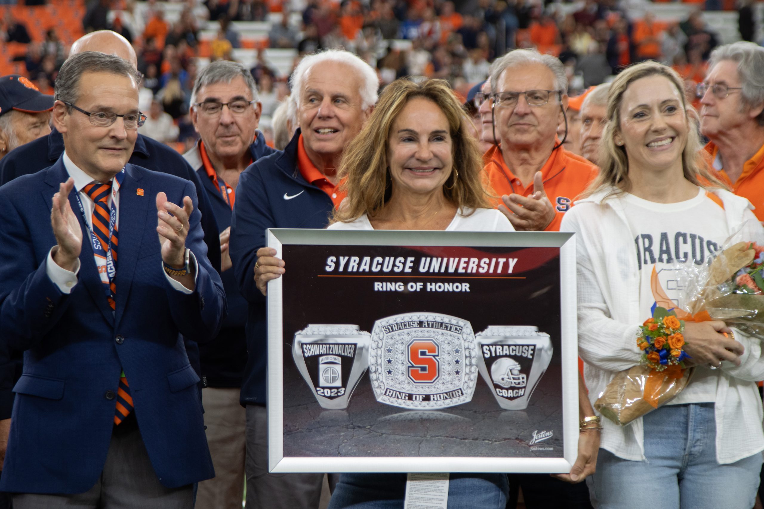 Individual holding a Rong of Honor plaque surrounded by other people on the field in the Dome. 