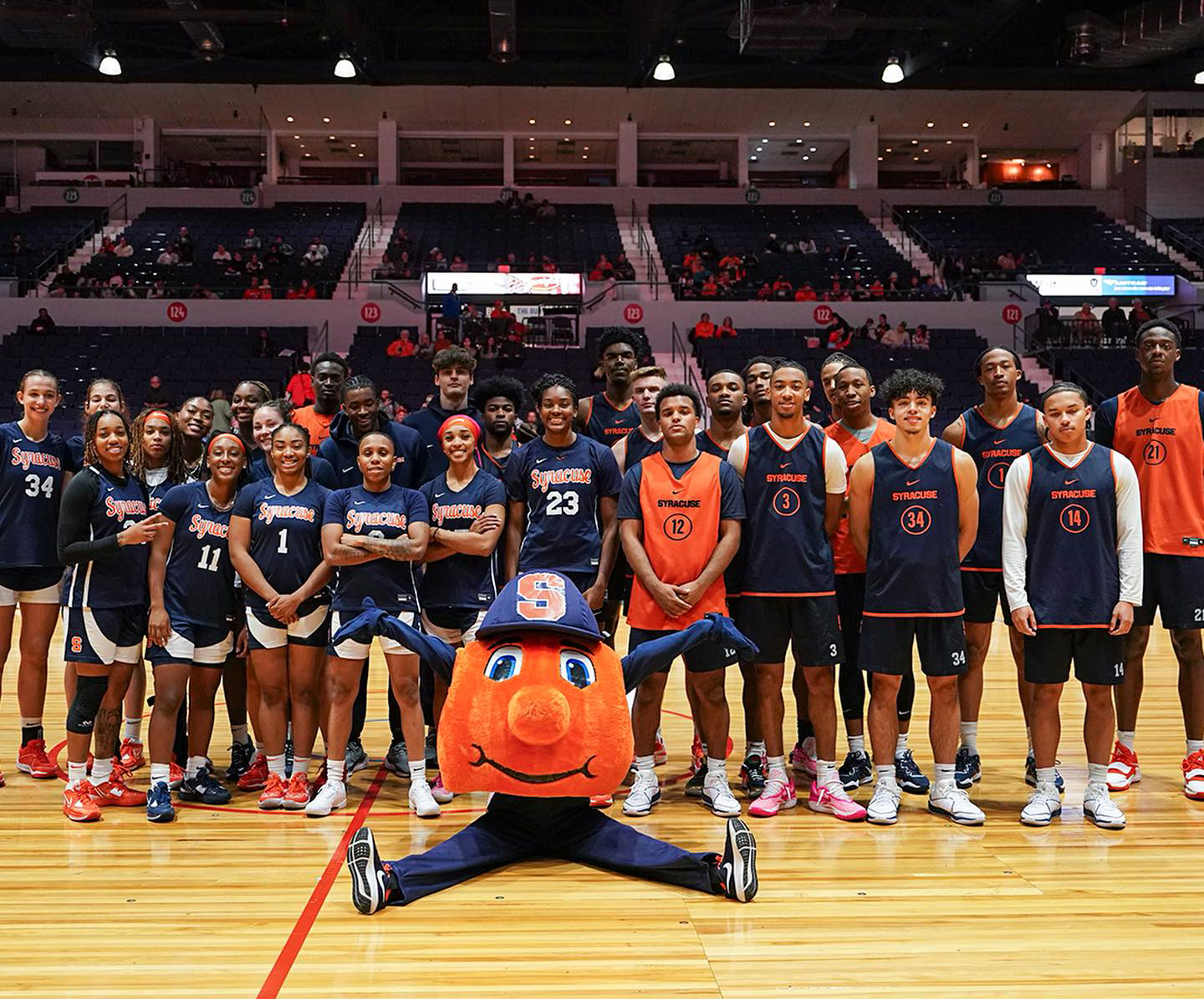 Men's and Women's basketball teams standing together on a court with Otto sitting in front of them