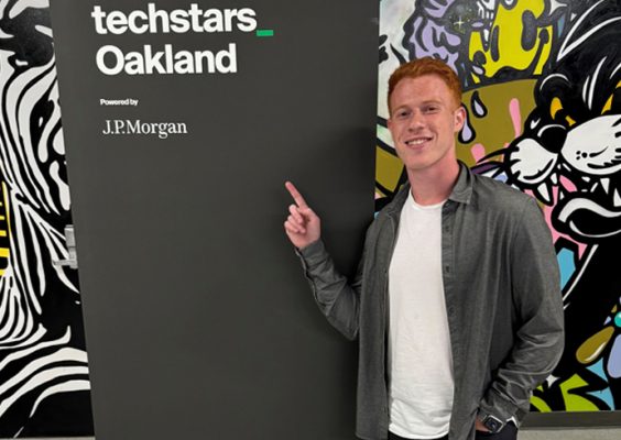 A man in a leather jacket points at a sign readign Techstars Oakland.