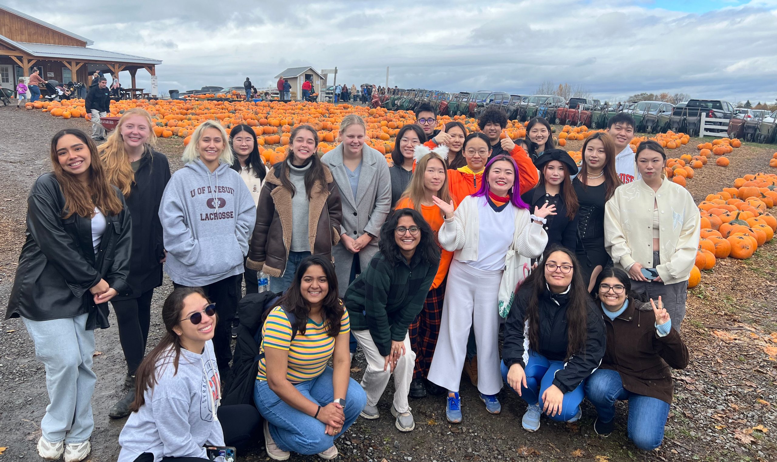 Group of students gathered together standing in front of a pumpkin patch.