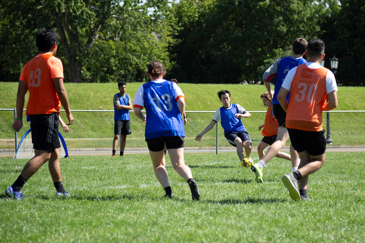 Several students wearing orange and blue jerseys playing soccer.