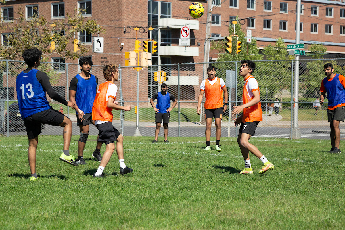 Several students wearing orange and blue jerseys playing soccer. 