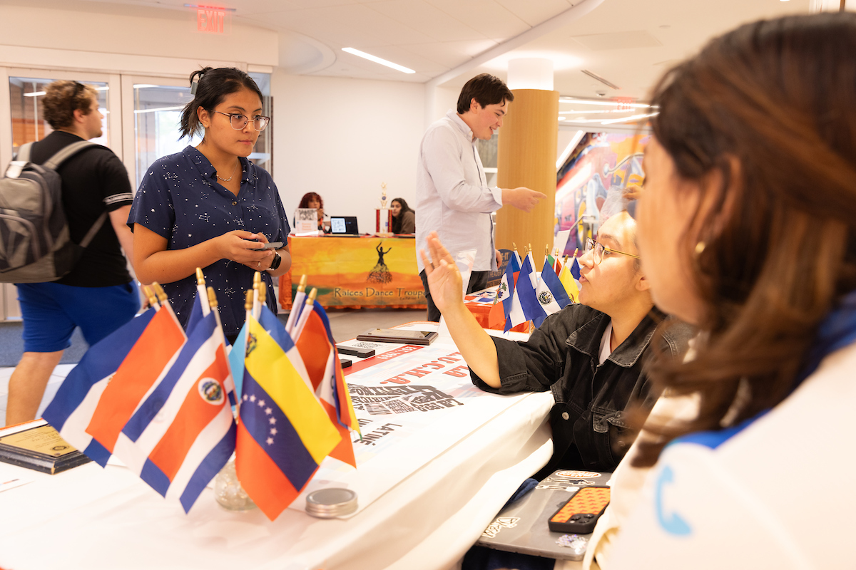 Two individuals sitting at table with flags on it talking to a student.