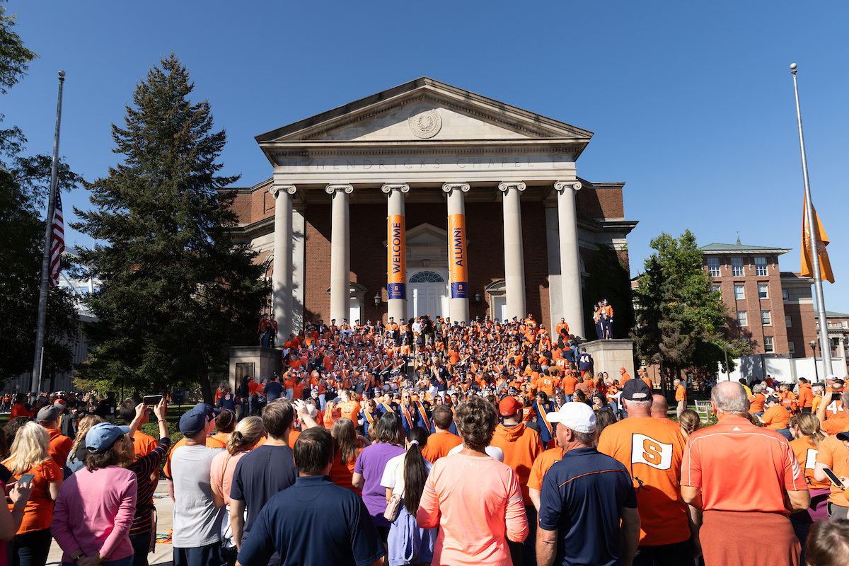 A large group of people gather in front of Hendricks Chapel where band is performing
