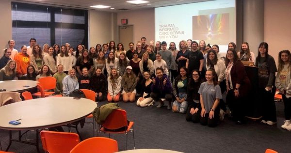 A group of students pose for a photo with a slide titled trauma informed care begins with you in the background.