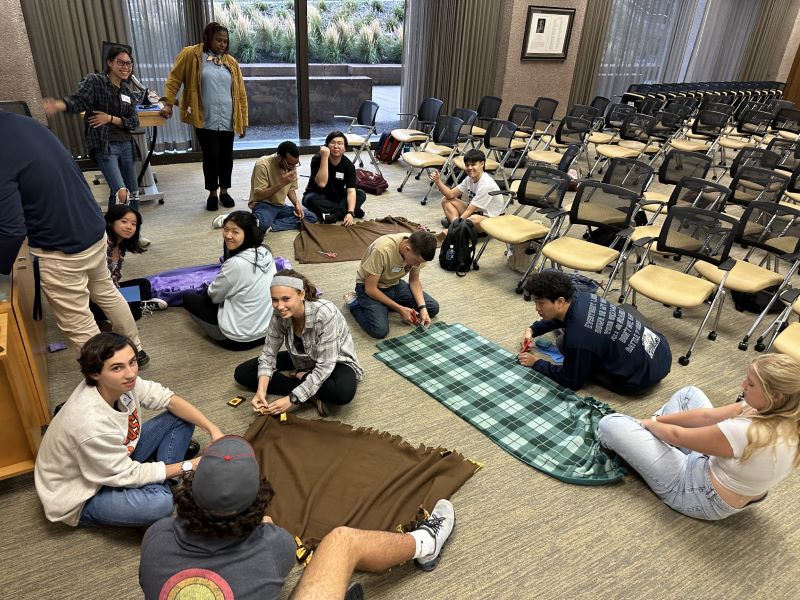 students rolling blankets on the floor that will be donated to a community group