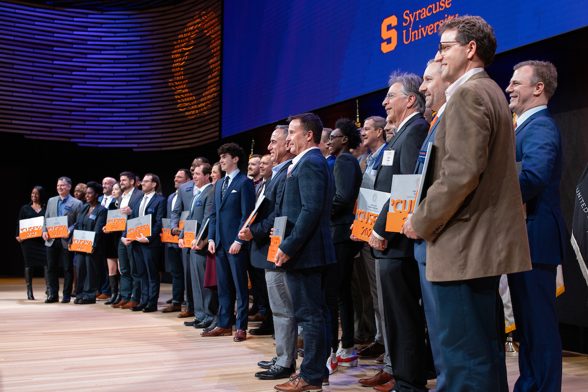 Large group of people gathered on a stage holding orange and white awards.
